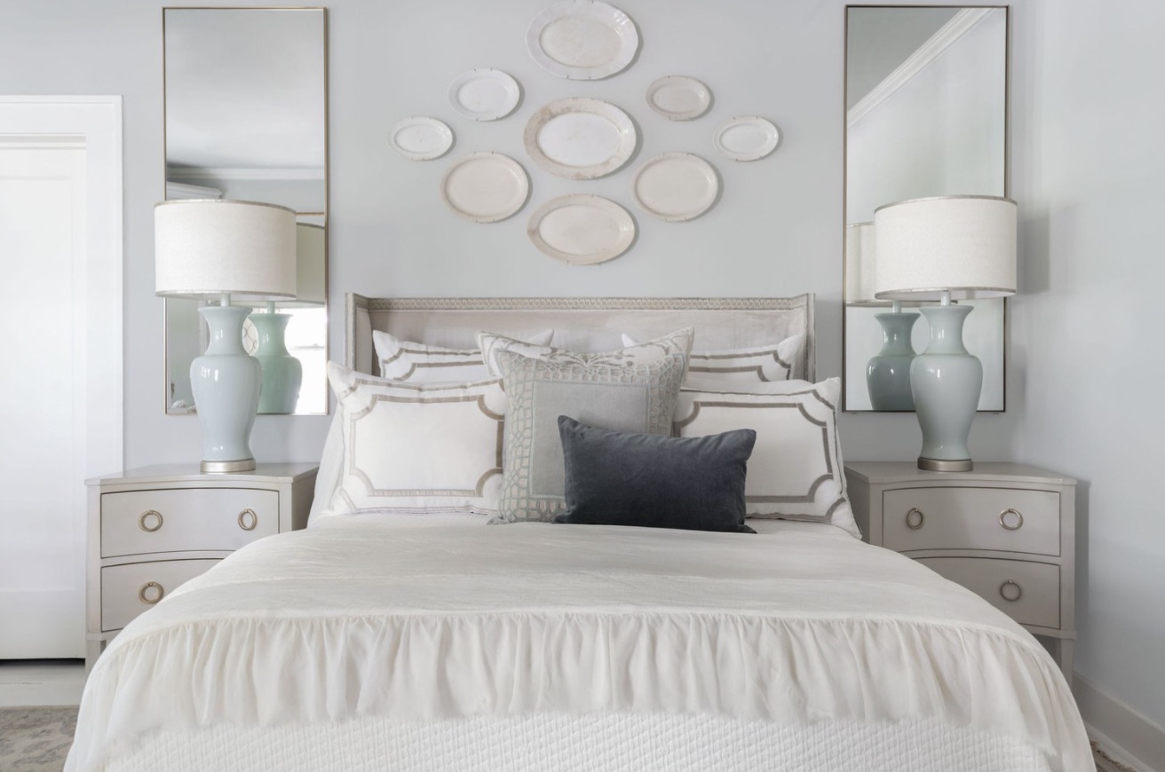 A serene bedroom with a white bed and a mirror, blending old and new elements in soft white, silver, and blue tones.