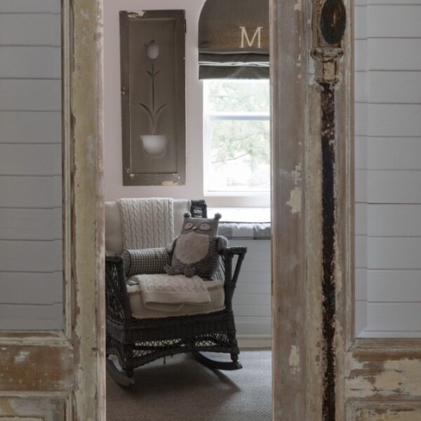 A vintage rocking chair by a window in a pink and grey nursery, with custom valance and antique shutter.