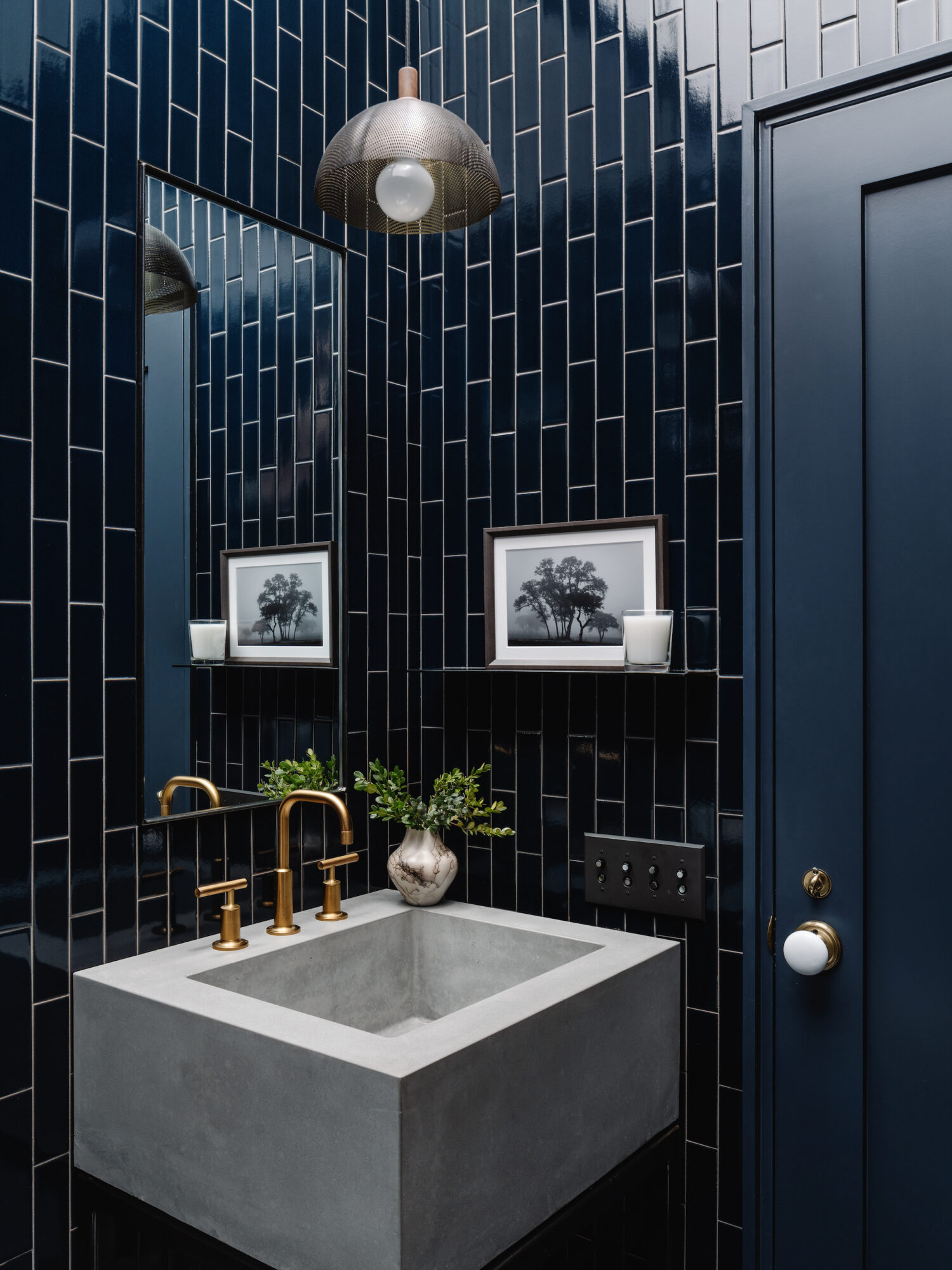 Navy blue tile powder room with cement sink and gold hardware.