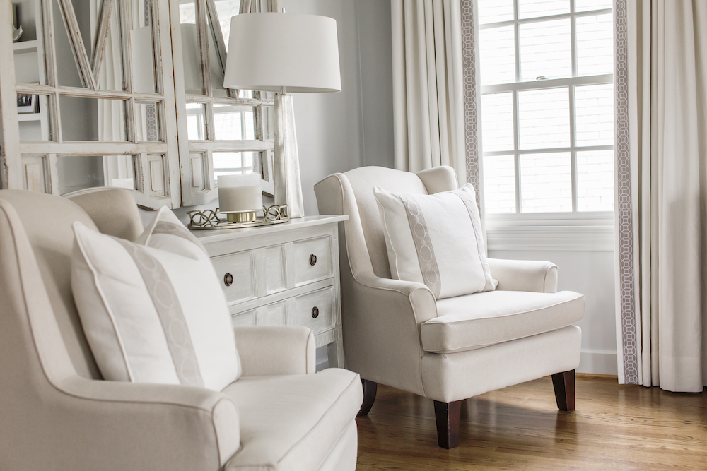 A pair of upholstered armchairs styled with luxe velvet trim pillows that play off the custom draperies with leading edge trim help create a sophisticated, but inviting sitting area.
