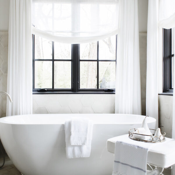 Stone hex tiles from floor to ceiling and a white porcelain tub are a vision of softness amongst the floor-to-ceiling sheers and relaxed window valances.
