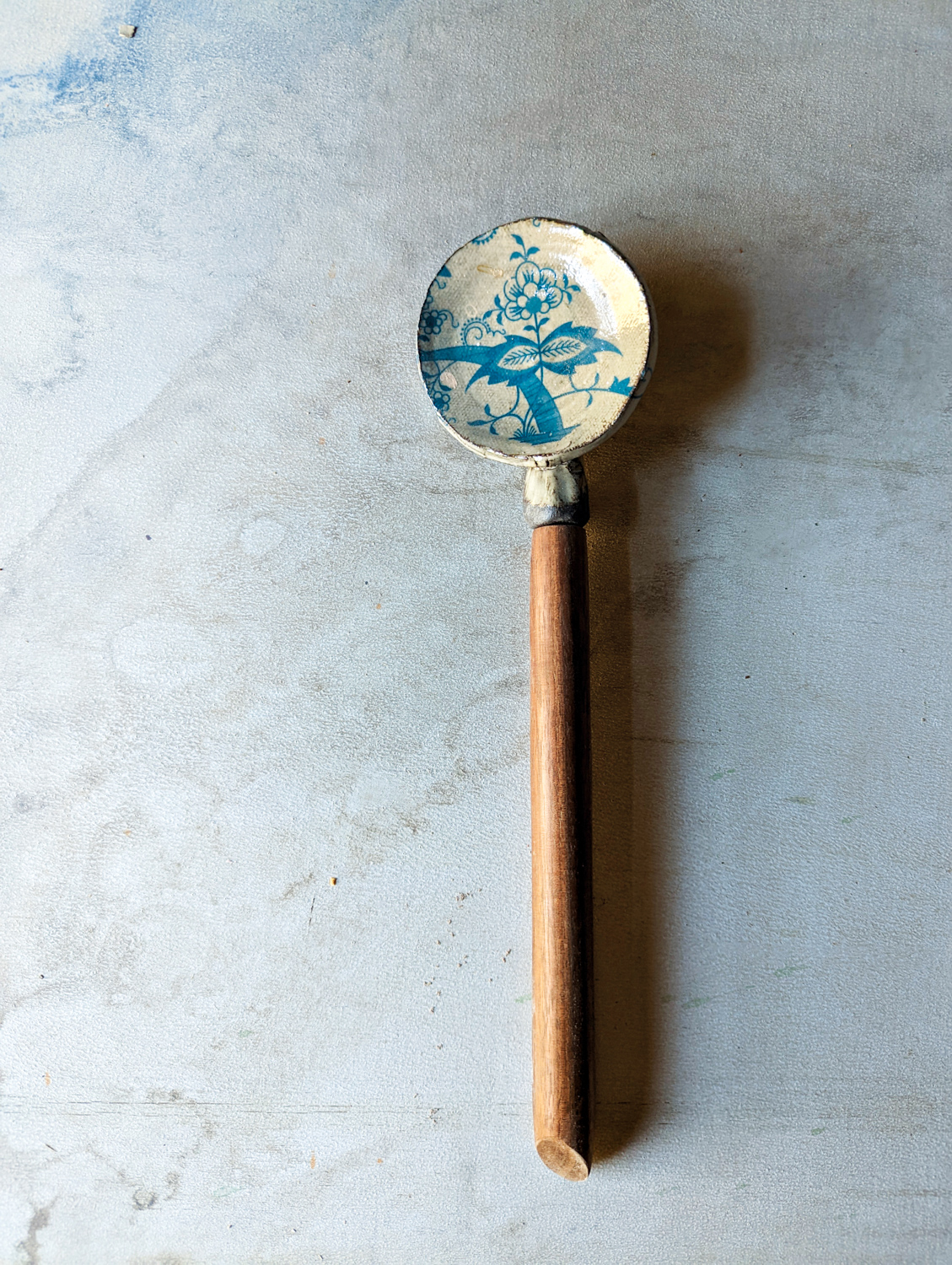 Ivory ceramic spoon with blue floral pattern and wood handle.