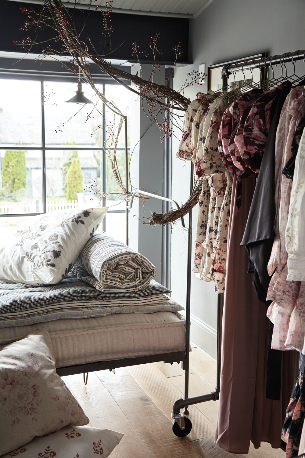 clothing racks and a banquette with pillows and rolled sheets by a window at the Huntress boutique