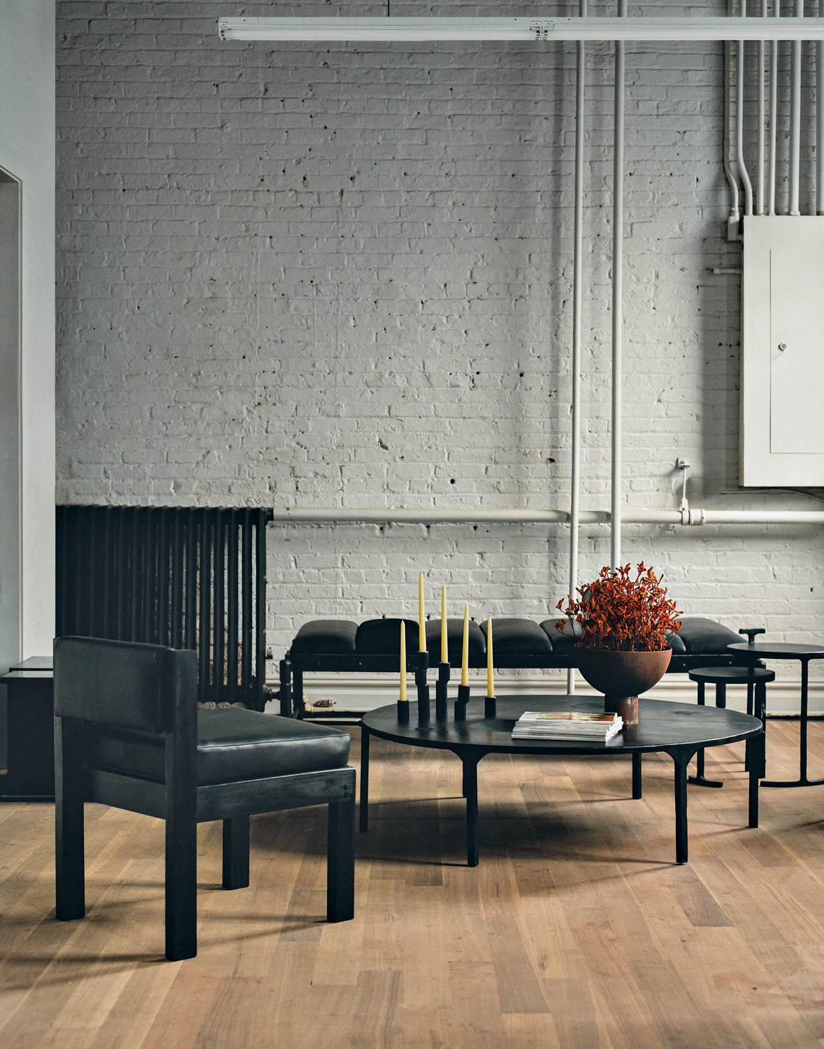 all-black coffee table, armchair and sofa against a brick wall painted white at the J.M Szymanski workshop and showroom