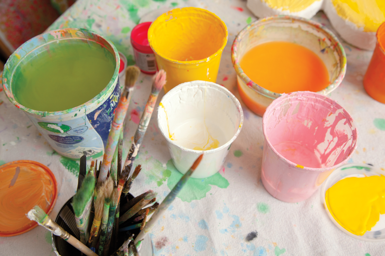 green, white, yellow orange and pink paint, and used painbrushes in cups