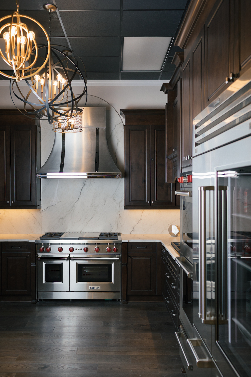 Brown Cabinets with large stainless steel appliance and metal lighting with wood floors