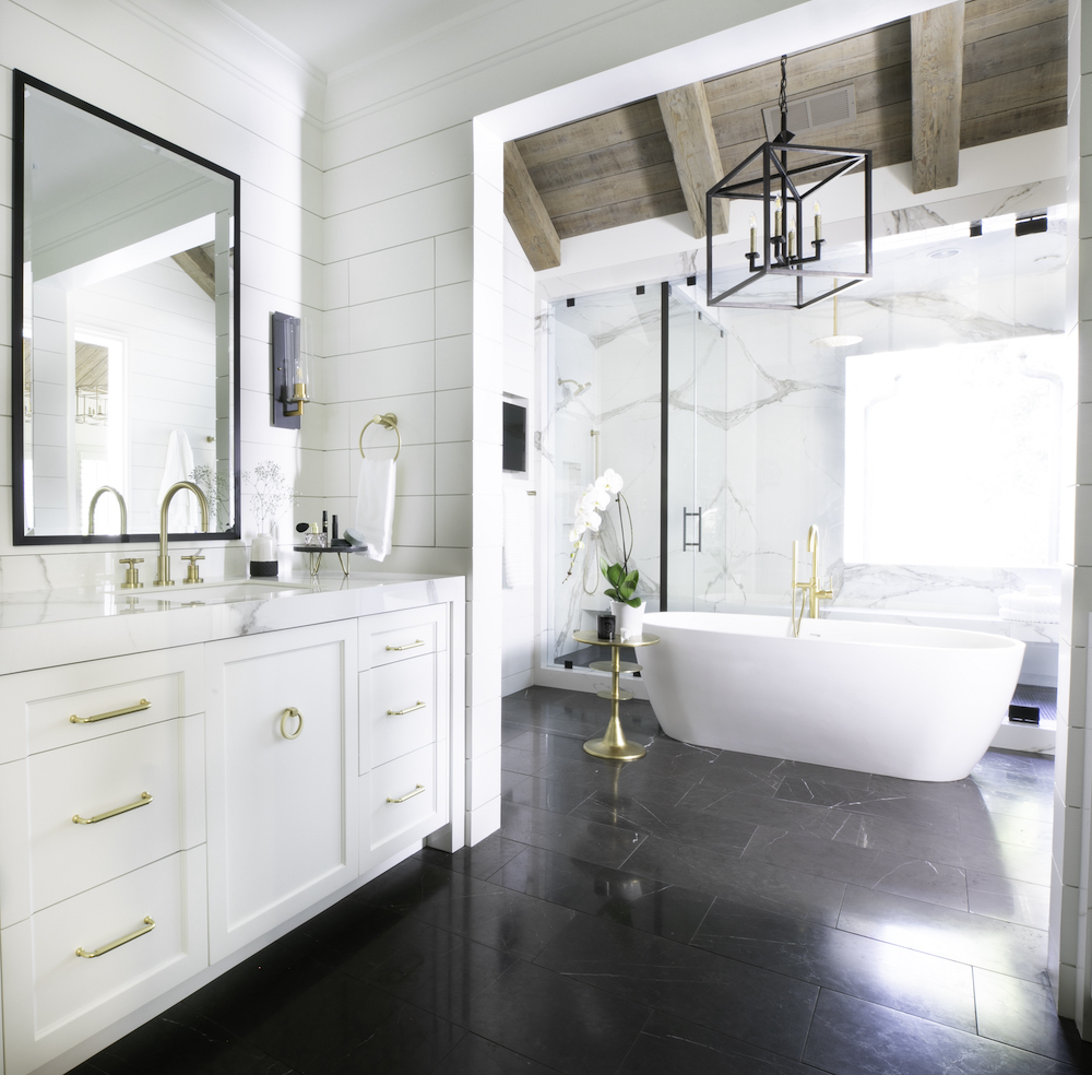 large bathroom with black tile flooring, white cabinets with gold hardware and fixtures, and a standalone white tub in Georgia by Construction Resources