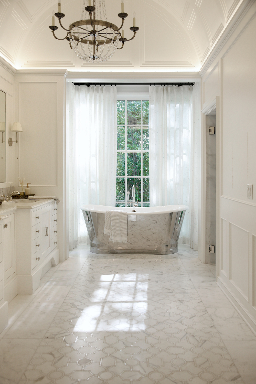 White bathroom with white tile and silver standalone tub with window and white drapes in home by Construction Resources in Georgia