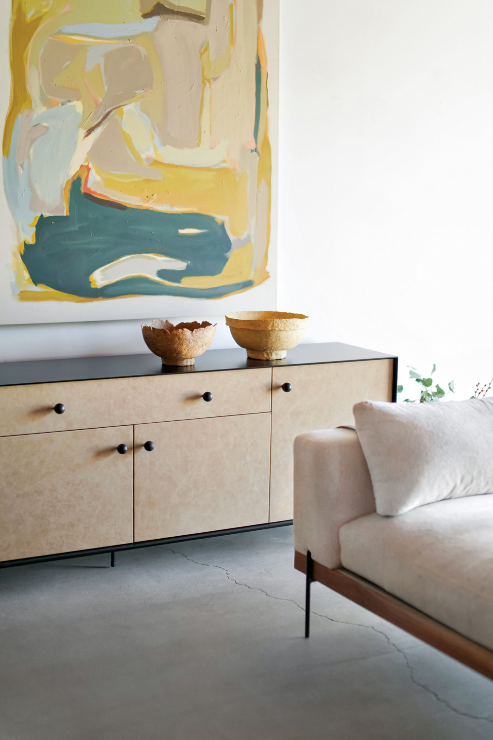 A couch and credenza underneath a large abstract painting