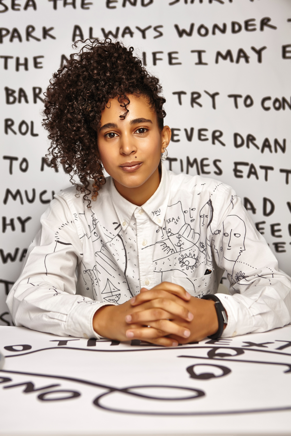 Portrait of Shantell Martin sitting in front of a mural of her art