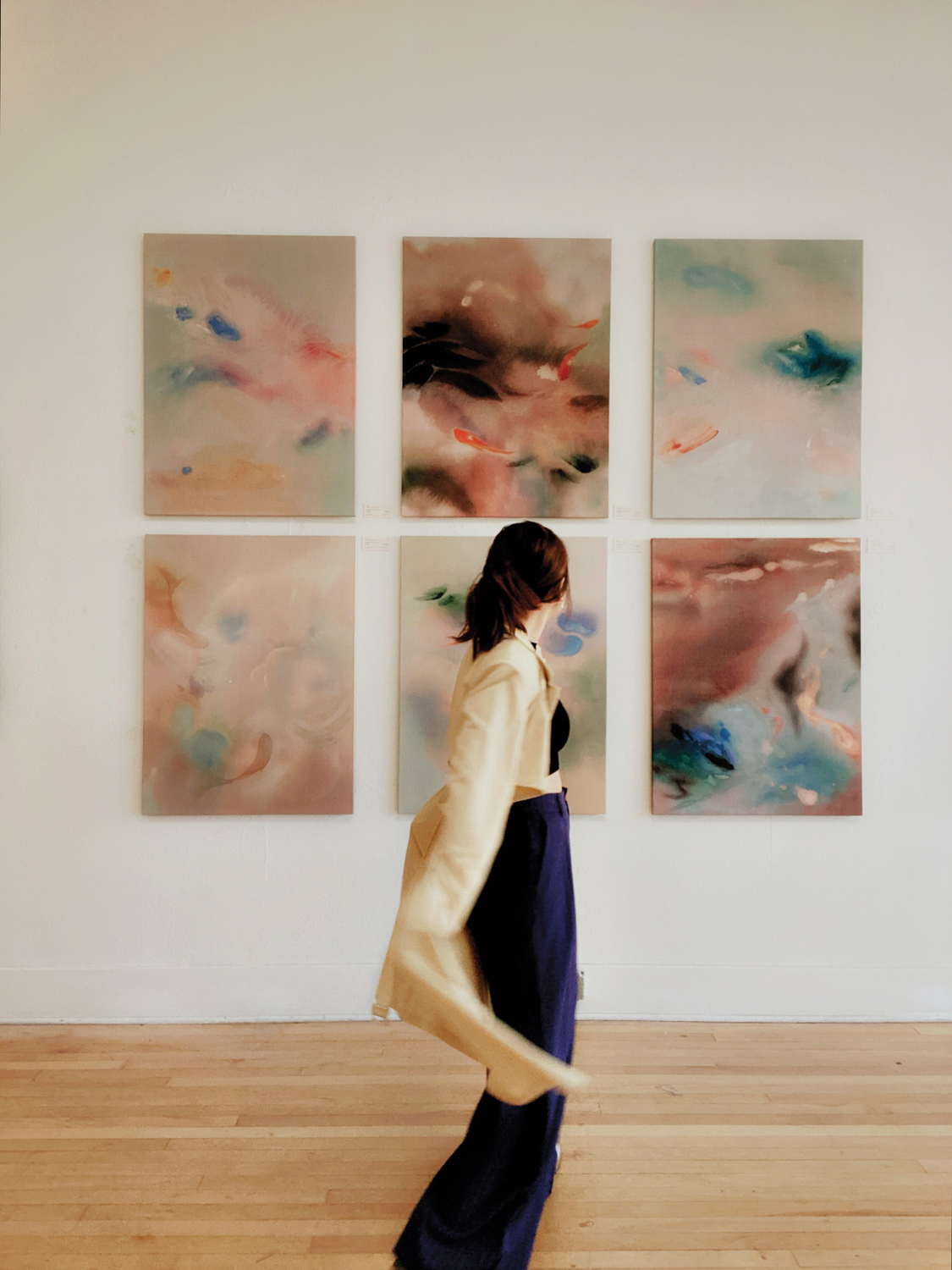 Artist AOTH standing in front of six of her abstract paintings