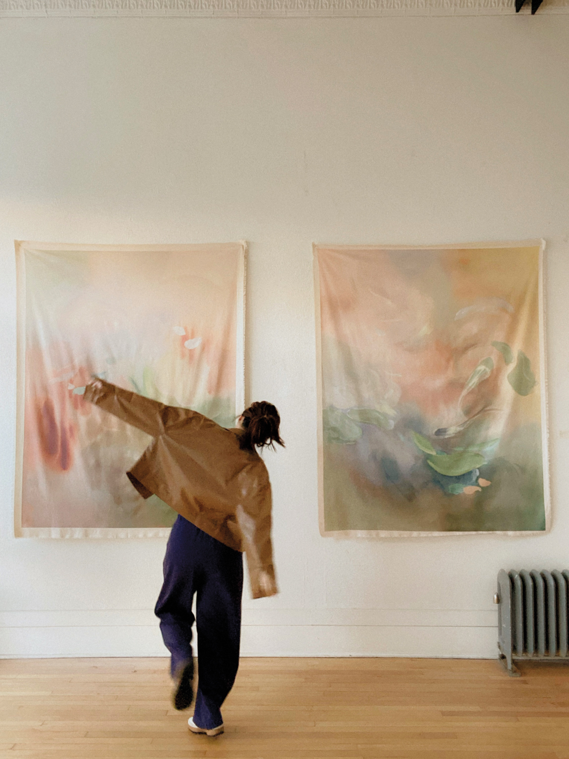 Artist AOTH standing in front of two of her artworks on fabric hanging loosely on a wall