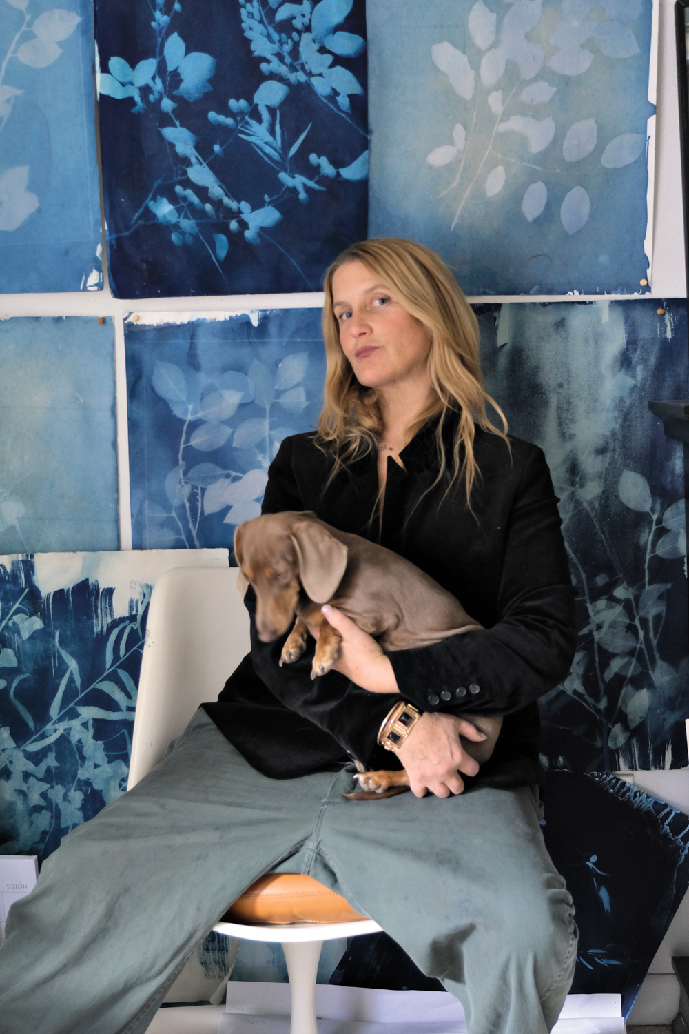 Edie Ure holding a Dachshund dog while sitting in front of swatches of her patterns in blue hues