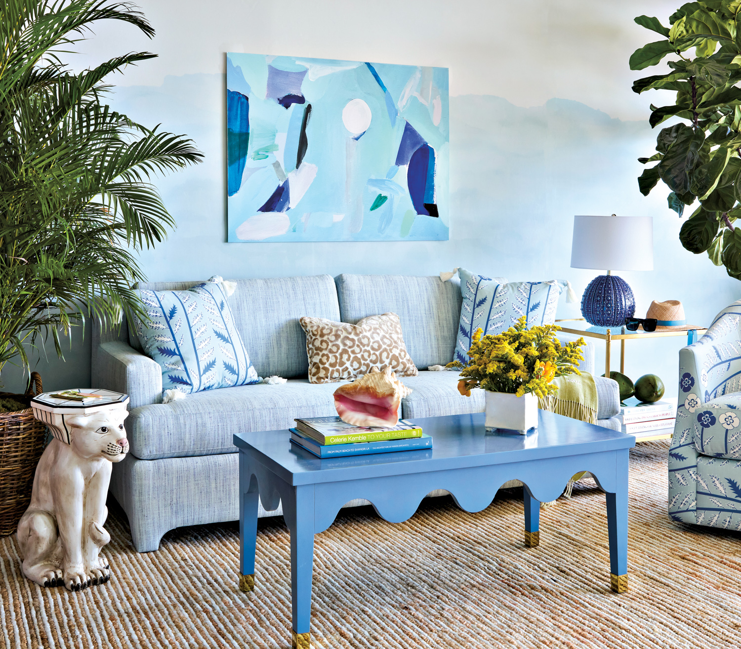 large plants flank suite living space with blue sofa, table lamp, armchair, table, walls and artwork