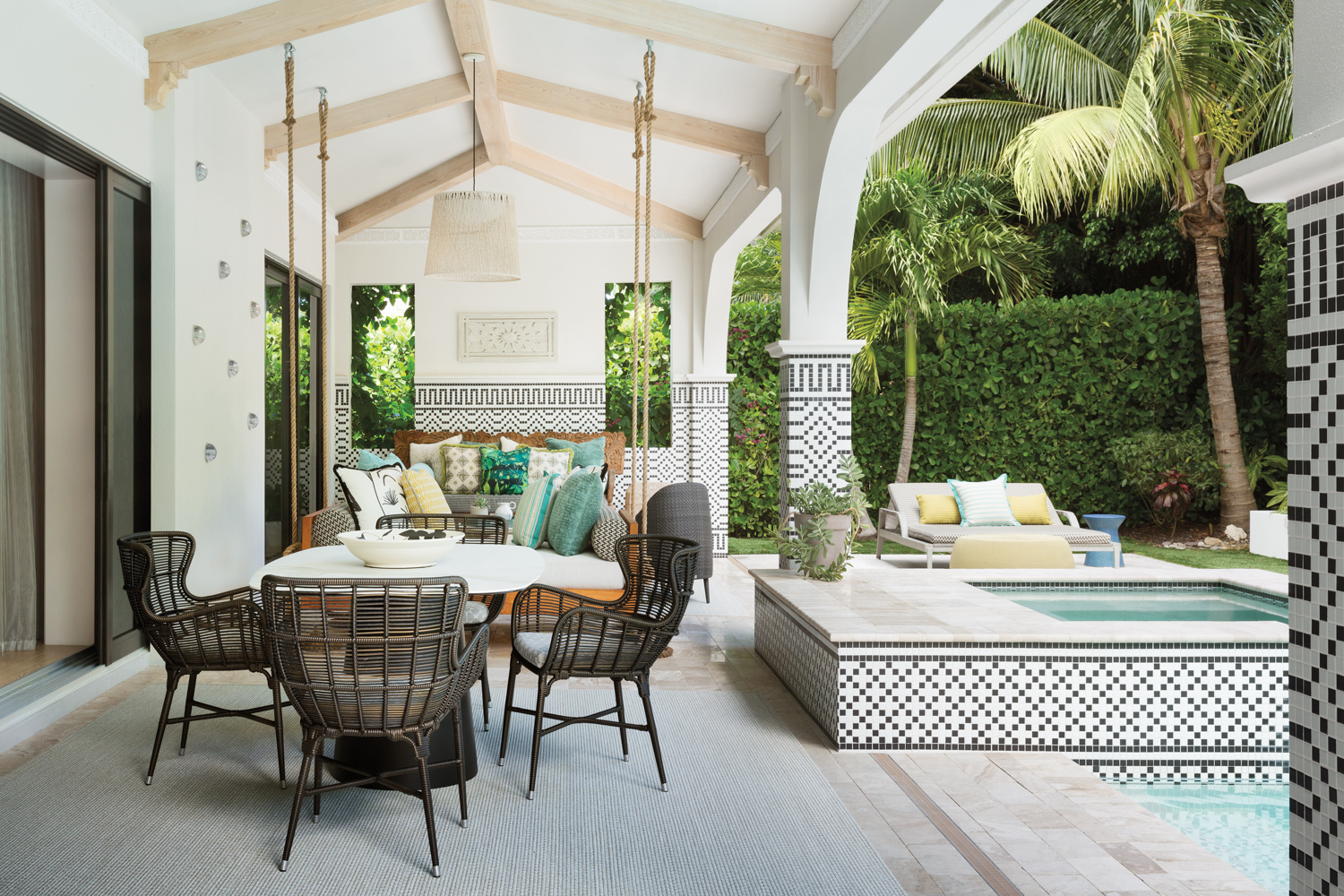 outdoor loggia with mosaic tiles, dining tables, black chairs, hanging daybed and pool