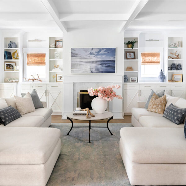 living room with two cream-colored sectionals, white walls and built-in, round coffee table and blue-toned rug