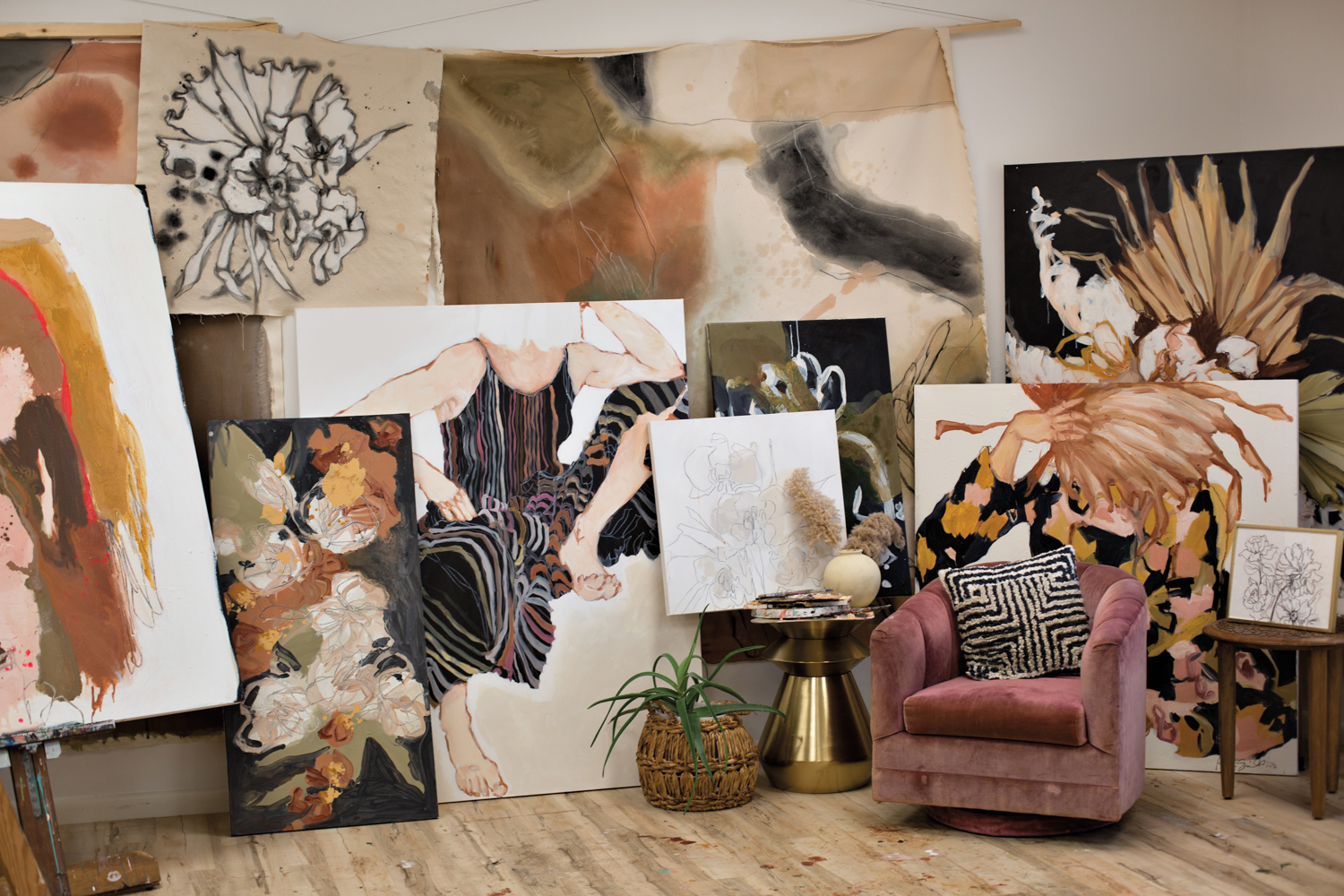 Assortment of Kristy Gammill artworks of various sizes against a white wall with a pink velvet armchair in front