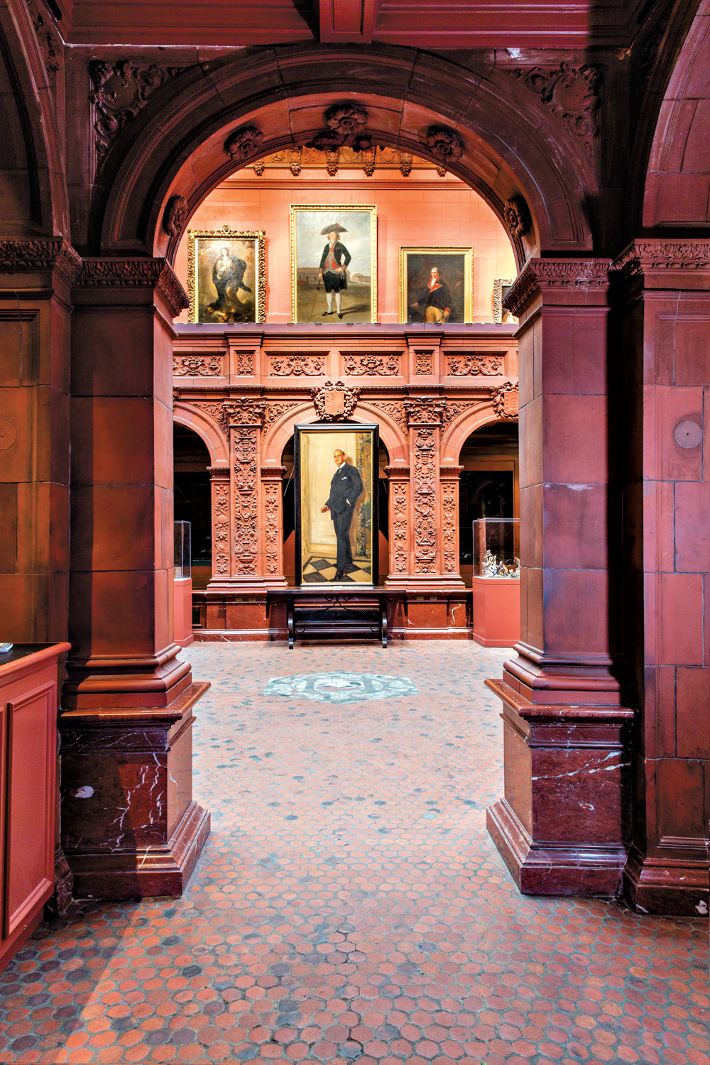 Tall paintings in gilded frames hanging between the red-marble arches of the Hispanic Society Museum and Library