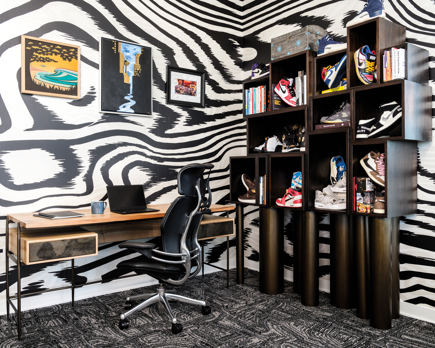 Home office with zebra-print wallpaper, a grey carpet and a black bookcase displaying sneakers