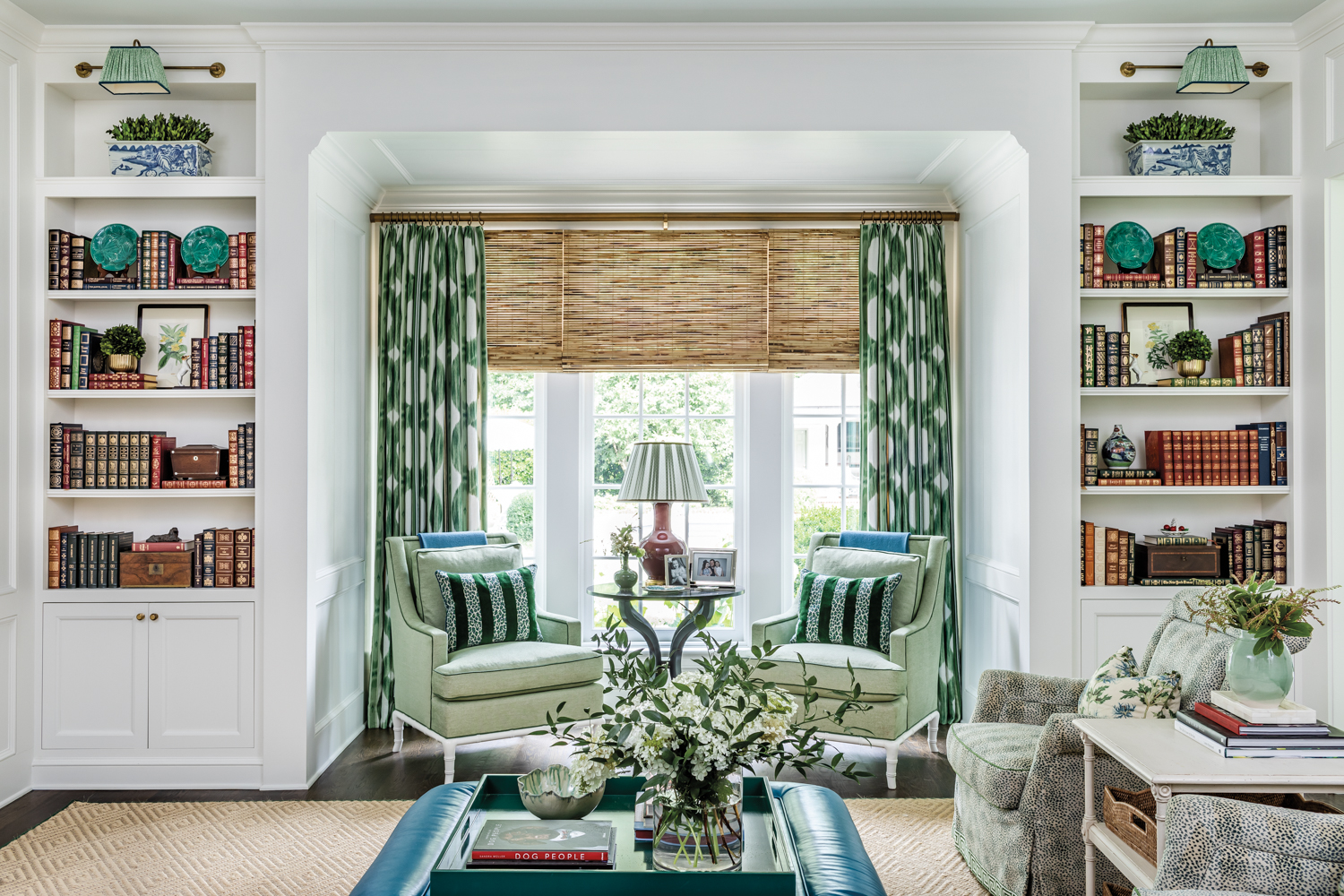 Keeping room with built-in bookshelves, patterned draperies, a pair of armchairs and a leather ottoman