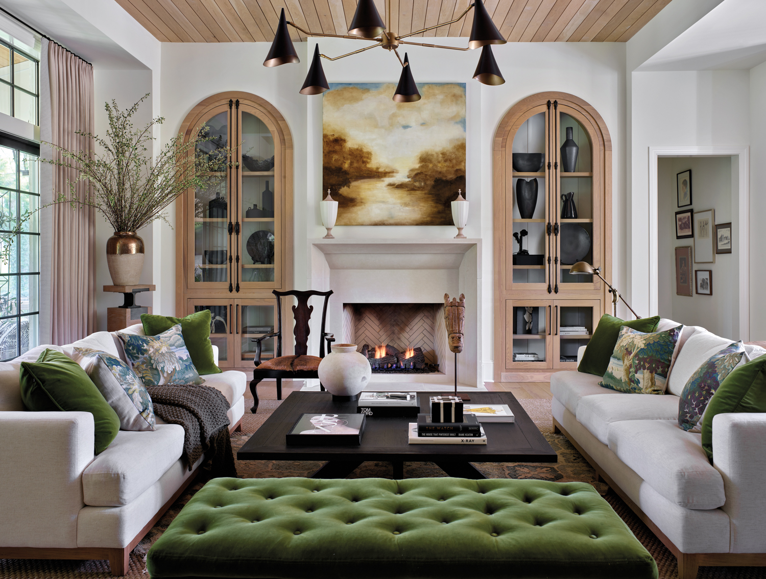 Living room with a pair of arched cabinets and sofas, a tufted green ottoman and a sepia-toned landscape painting