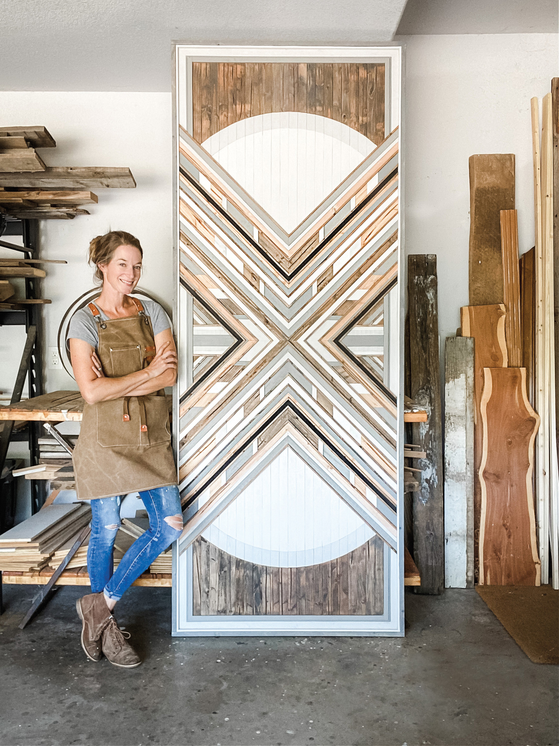 Ryan Renner leans against a floor-to-ceiling wood mosaic with her arms and ankles crossed