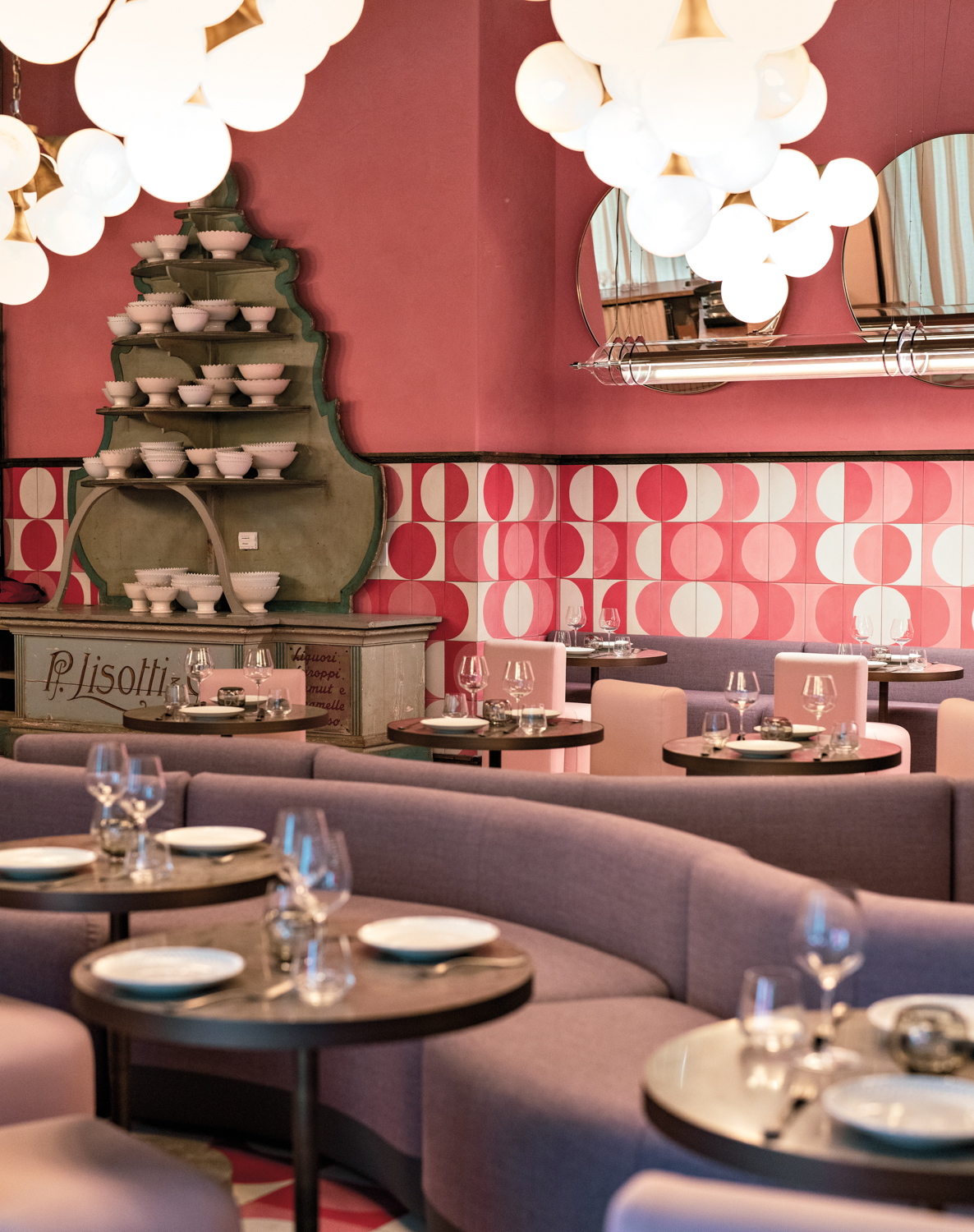 Curved banquettes and round tables create seating backed by pink walls and pink-and-white tiles