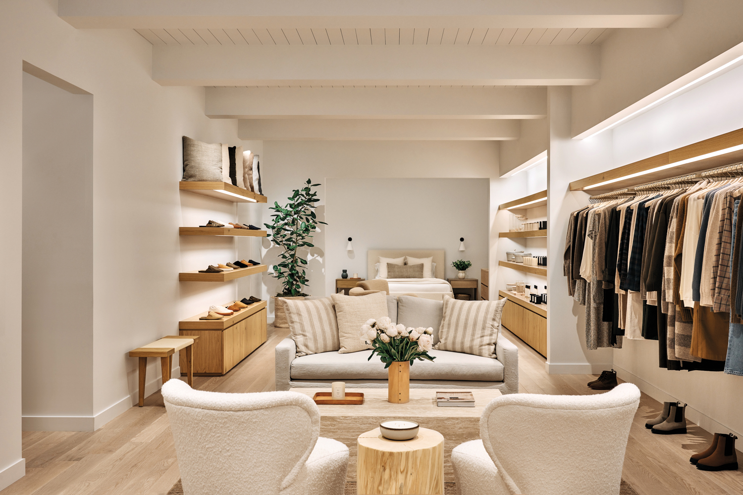 Jenni Kayne showroom with cream-colored sofa, armchairs, rack of clothes and wood display shelves