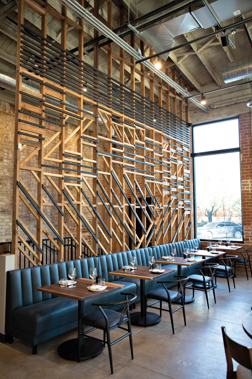 Rows of restaurant tables facing a wall-long leather banquette against an intricate wood-carved wall