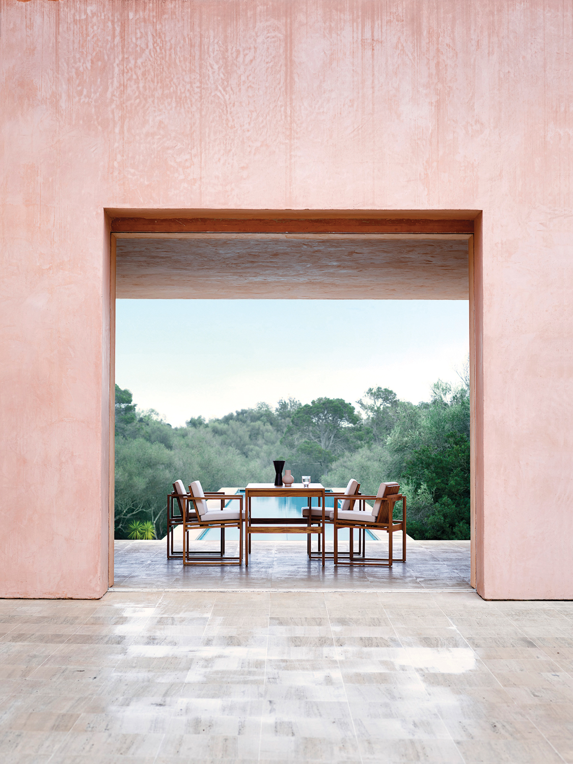 Exterior photo of a dining table and chairs under a pink arch with a swimming pool in the distance