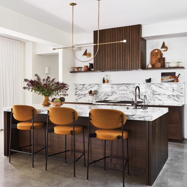 kitchen with a slatted-wood hood cover, marble counters and backsplash, a brass-and-white-leather pendant sand three counter height stools
