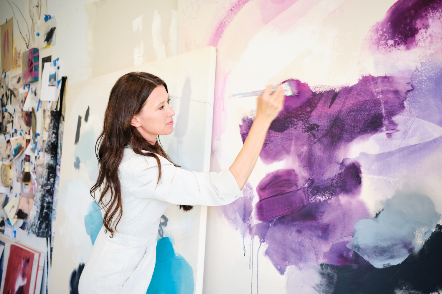 Melissa Herrington holding paintbrush against large canvas with purple abstract images