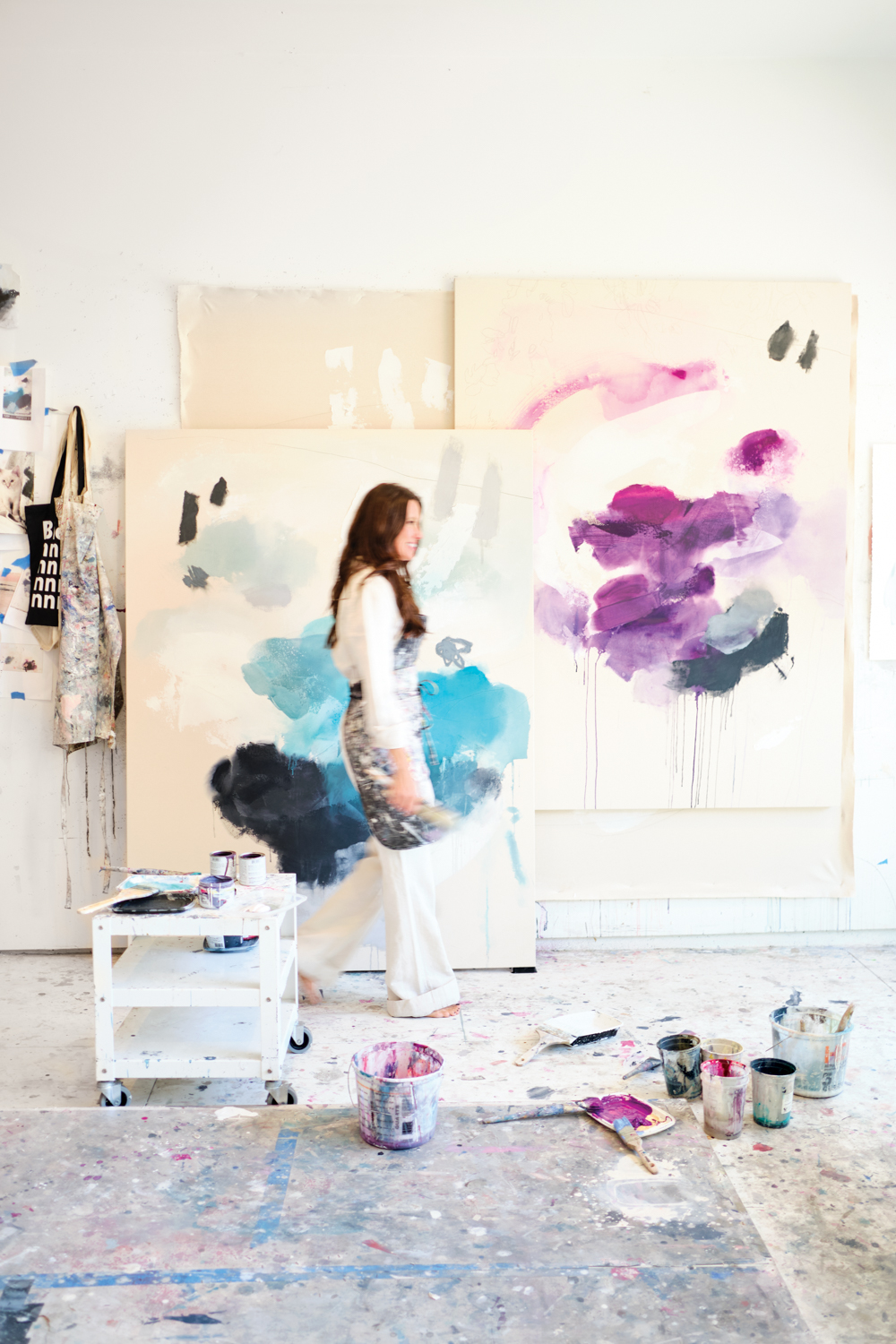 Melissa Herrington walking through art studio filled with large abstract paintings and canvases