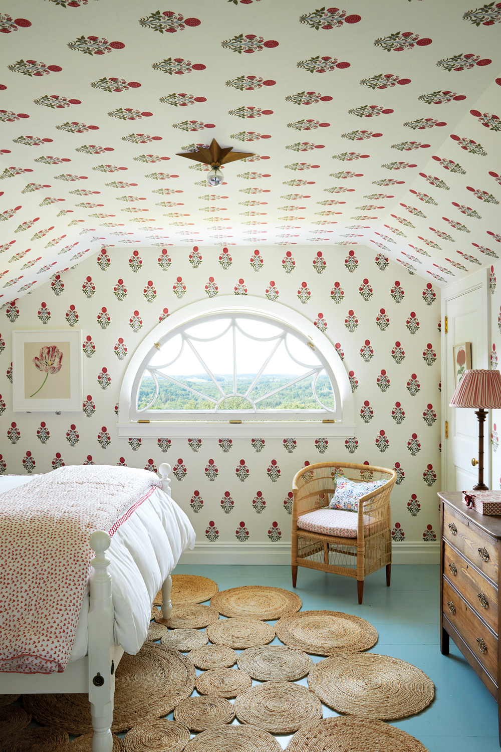 Bedroom with vaulted ceiling, patterned wallpaper and semi-circle-shaped window, with a bed and rattan chair