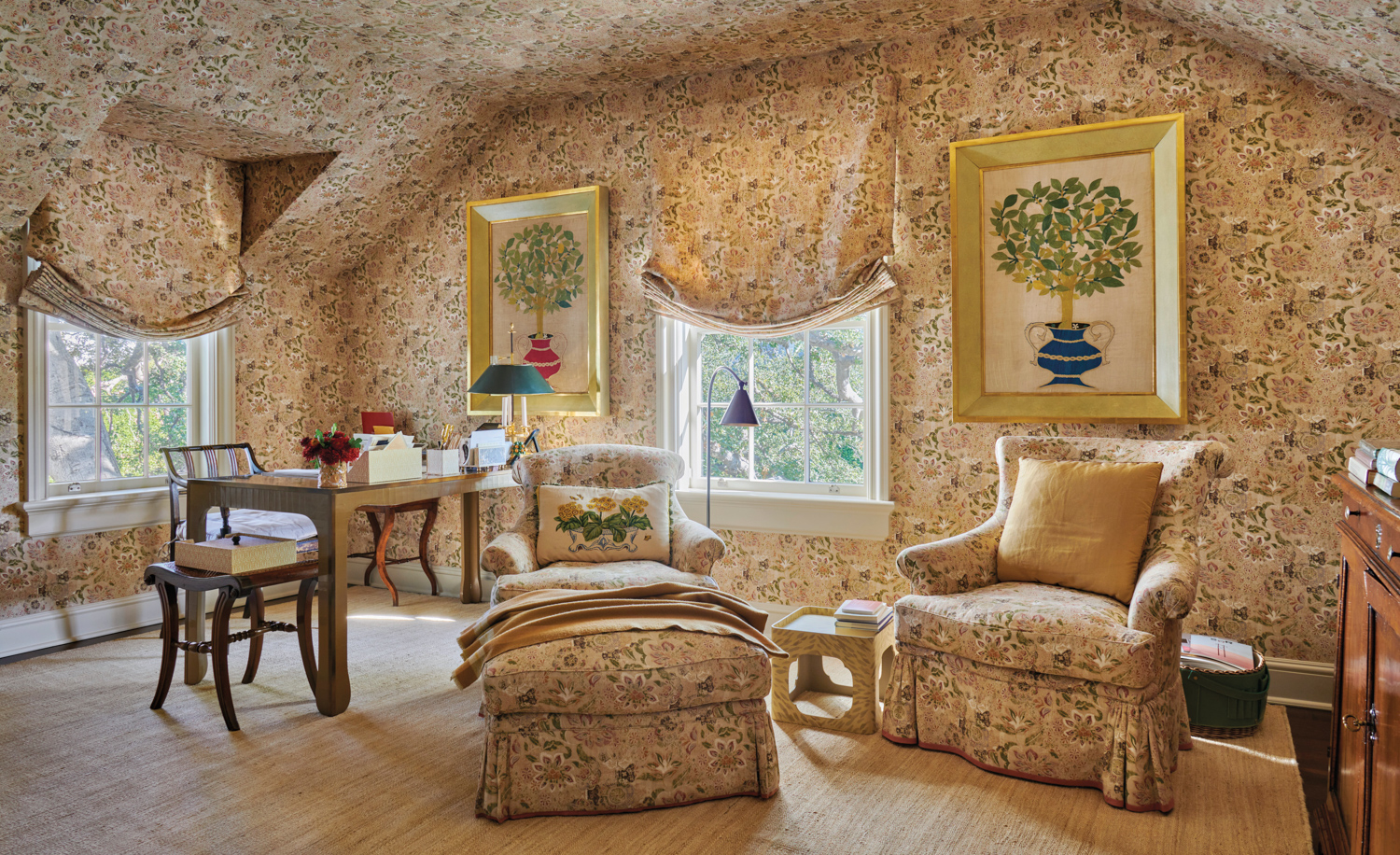 Room designed by Suzanne Rheinstein with patterned wallpaper, window treatments, armchairs and ottoman. A wooden desk and chair are in the corner.
