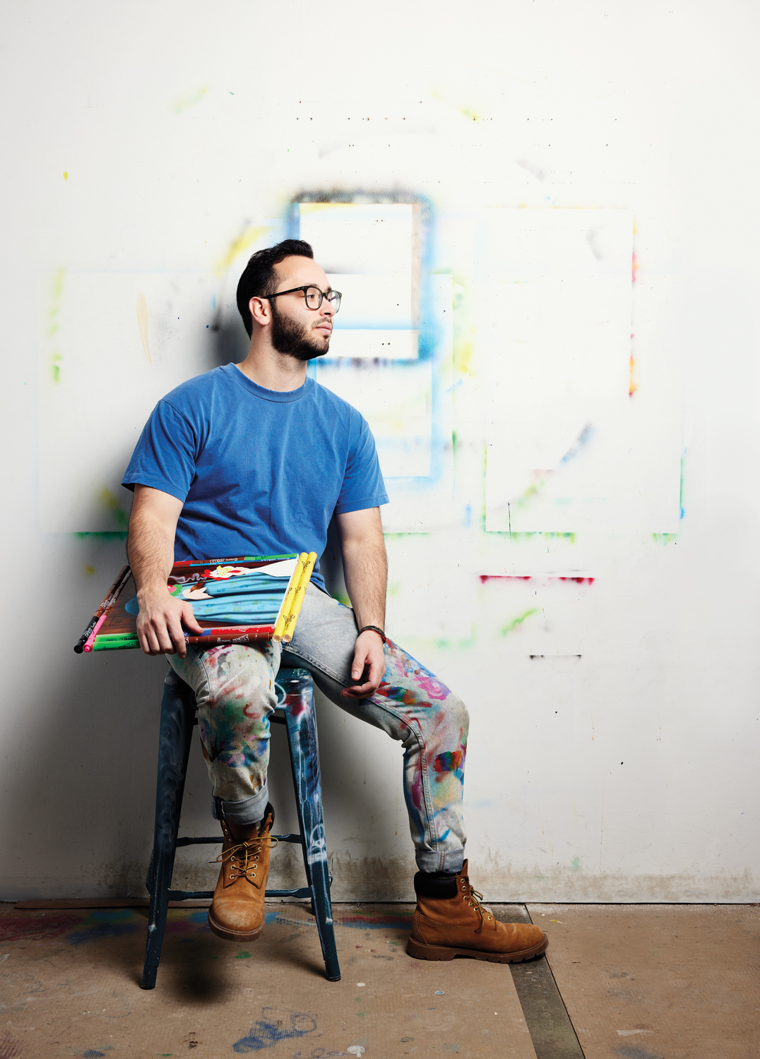 Griffin Goodman in blue t-shirt sitting on a stool holding a painting