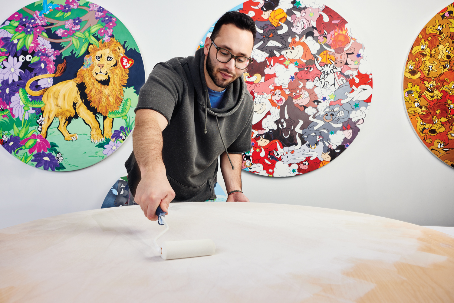 Griffin Goodman using a paint roller on wood in front of three circular paintings