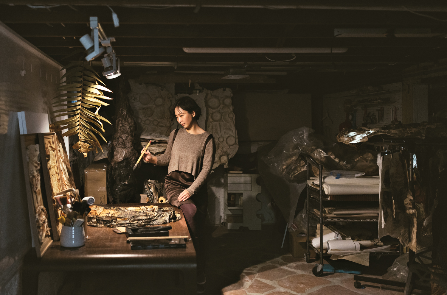 A Korean-American artist stands in her art studio holding a paintbrush