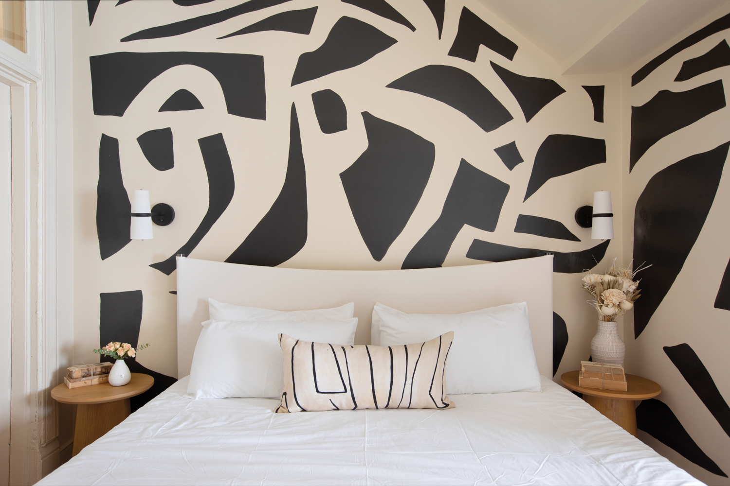 A black-and-white graphic mural by Magik Studios on the wall behind an all-white bed