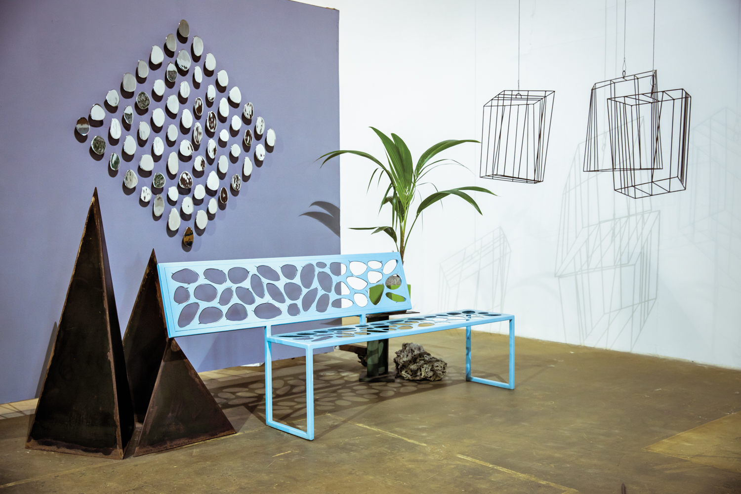 Carolina Sardi pieces displayed on steel wall with blue bench and plant