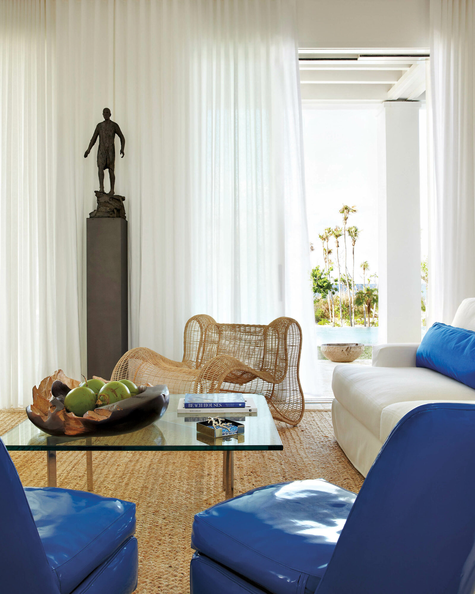 Room with blue armchairs, a lacquered coffee table, a curved rattan armchair and a statue of a man
