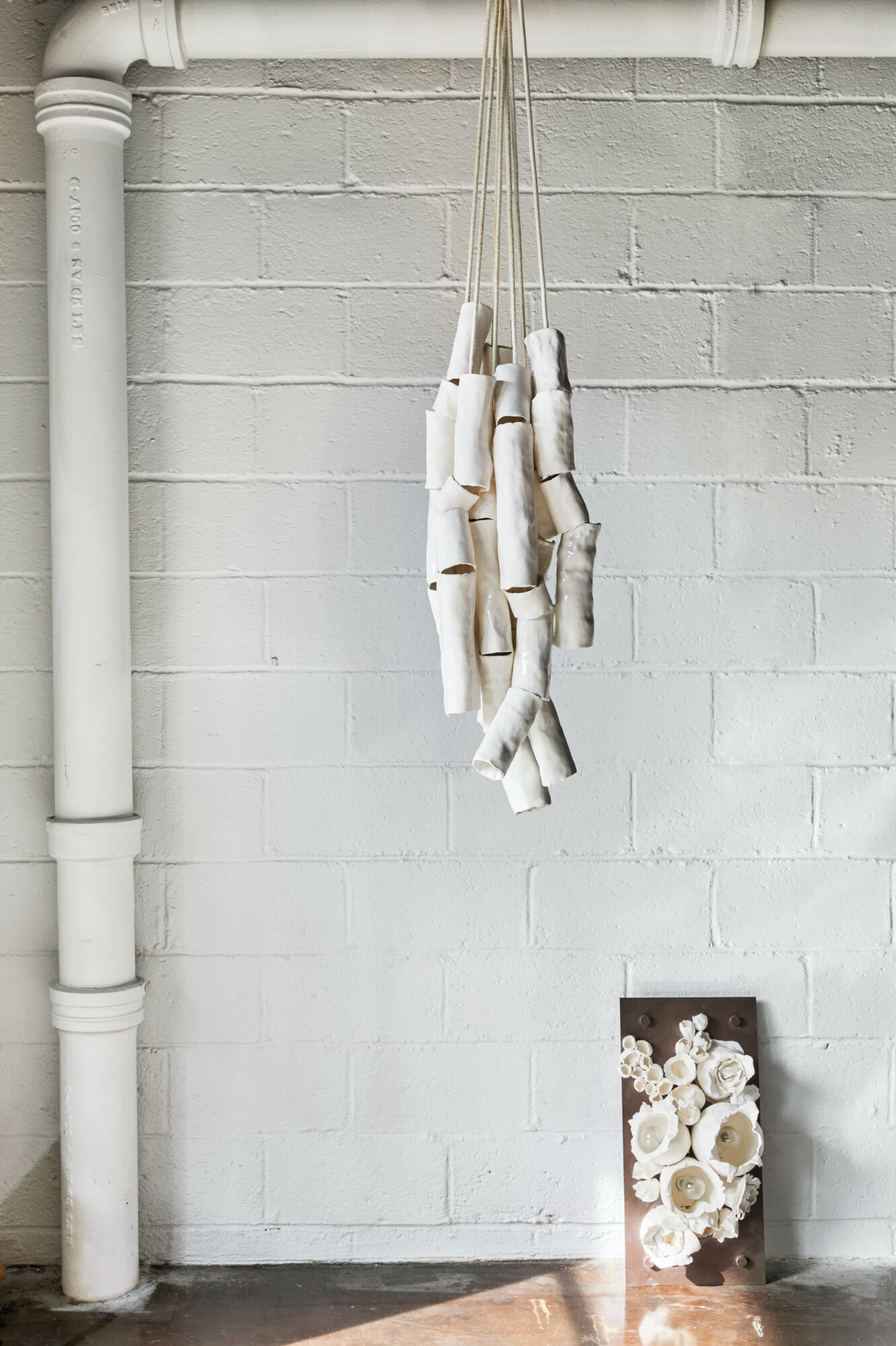 Stoneware sculpture hanging from the ceiling and a three-dimensional work leaning against the wall