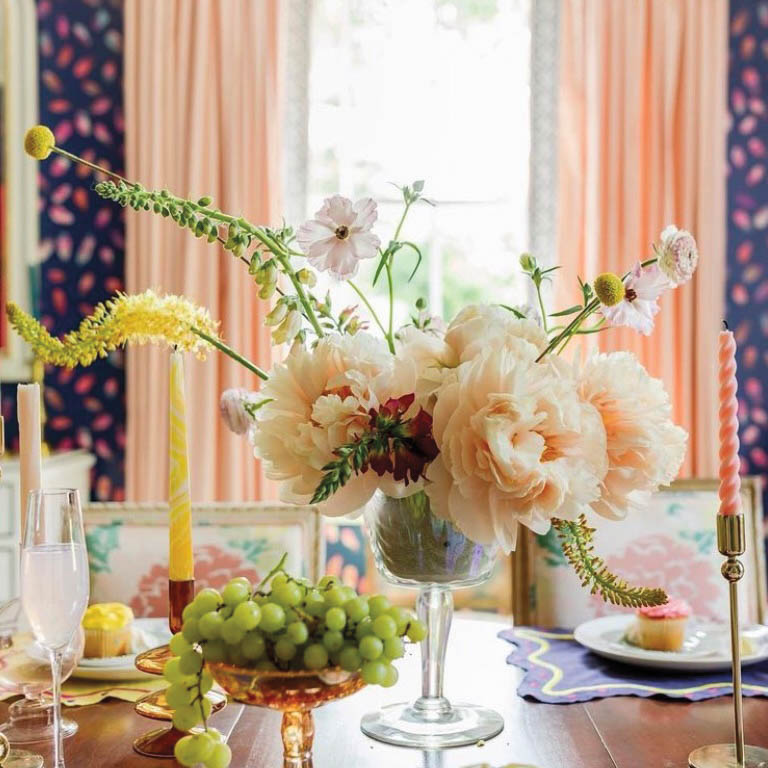 White floral arrangement atop a dining table set with colorful taper candles, by Colson Horton