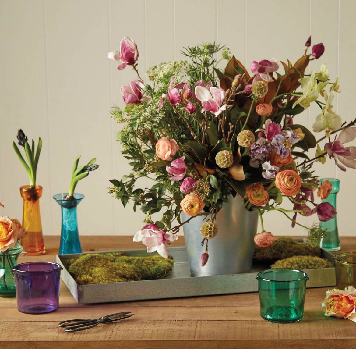 Pink and orange floral arrangement in tin pot atop a wooden table in feed by Colson Horton