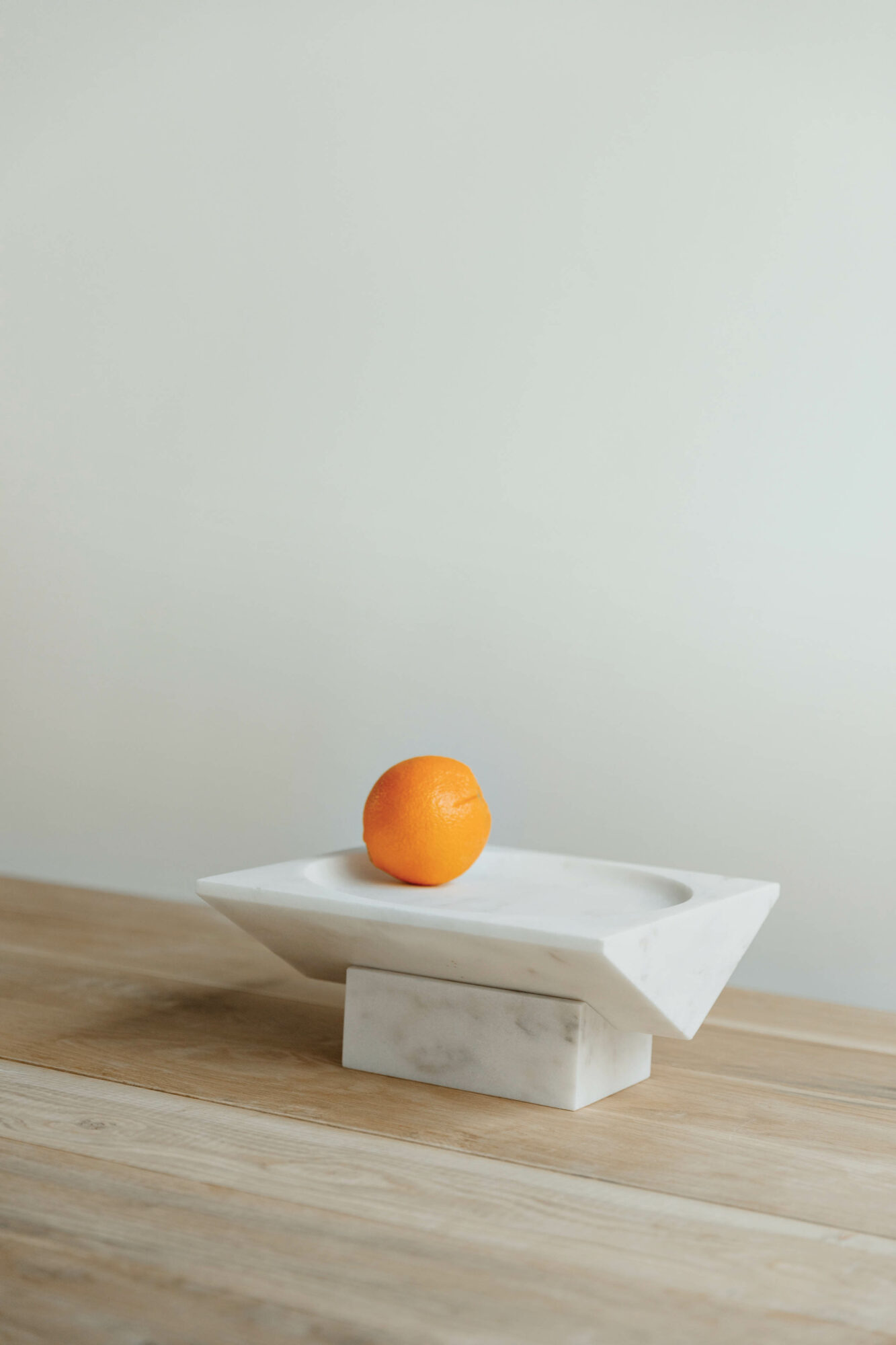 An orange on a clean-lined white-marble tazza, by Peter Fleming, on a wood surface