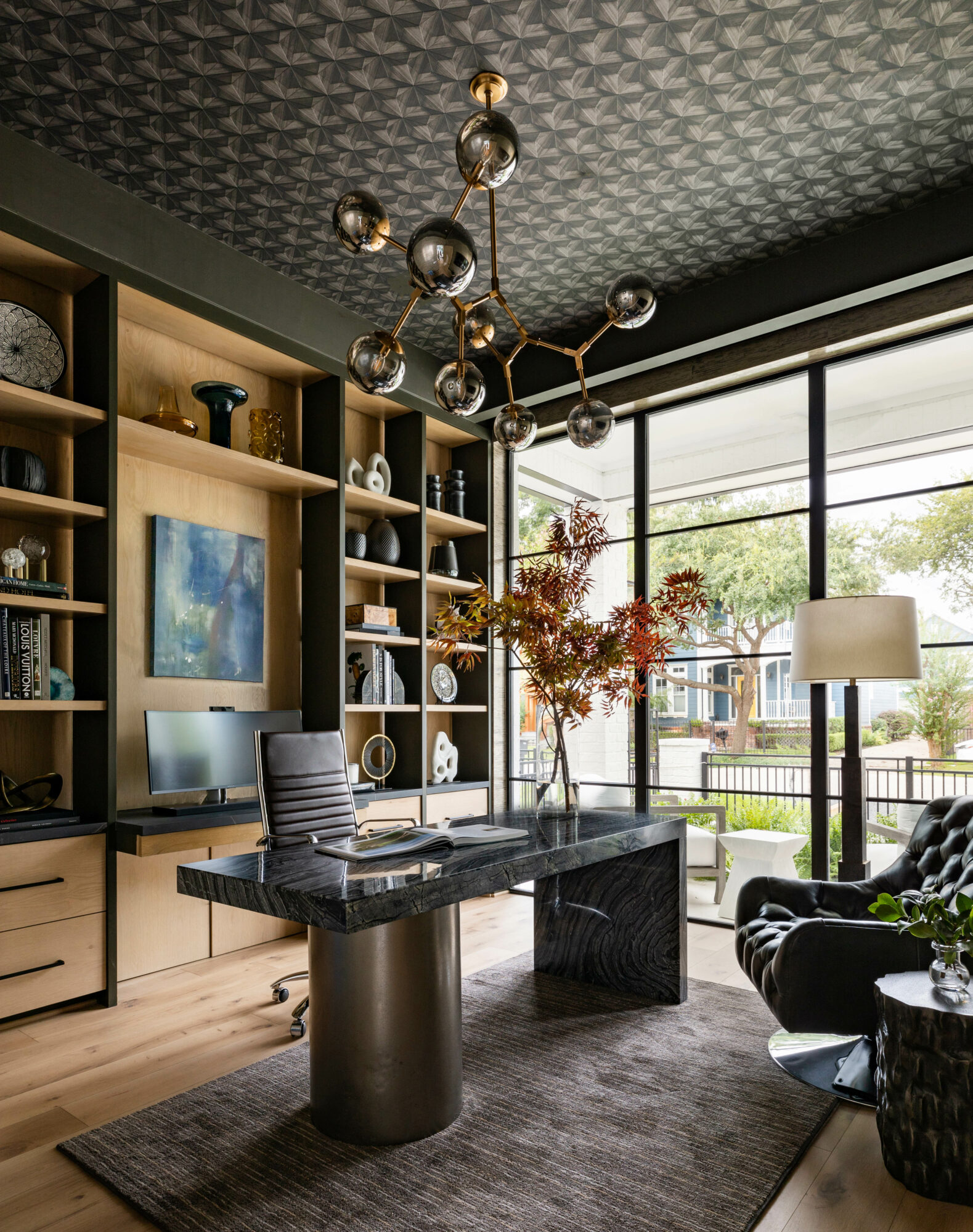 Study with black wallpapered ceiling, black armchair and desk, large windows, shelves and chandelier