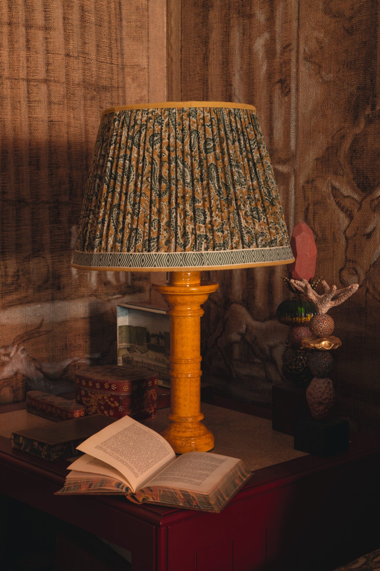 Oka x Cabana Lamp with pleated lampshade sitting on a table next to an open book