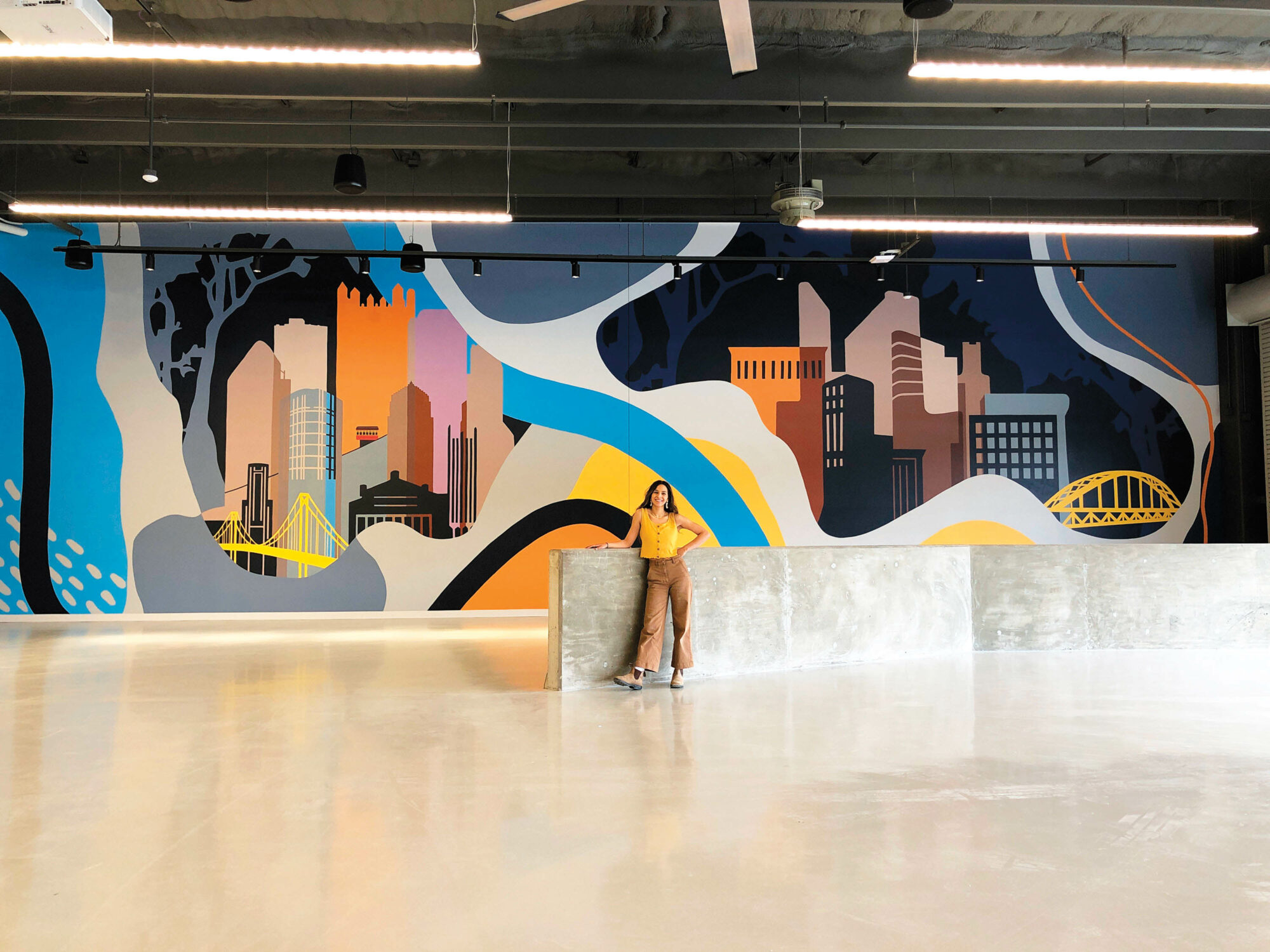 Artist Nicole Poppell standing in front of her mural of the Pittsburgh skyline