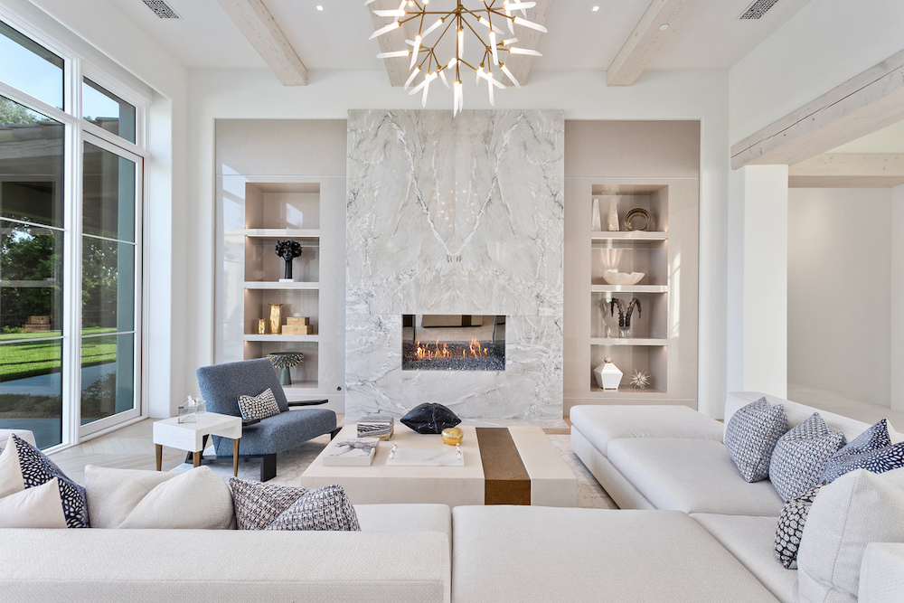modern living room in Southern California home with white sectional couch, blue accent pillows and chair and marble fireplace.