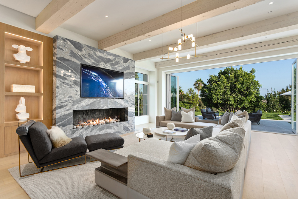 Living room in Southern California home with marble fireplace, gray sectional and built in cabinets.